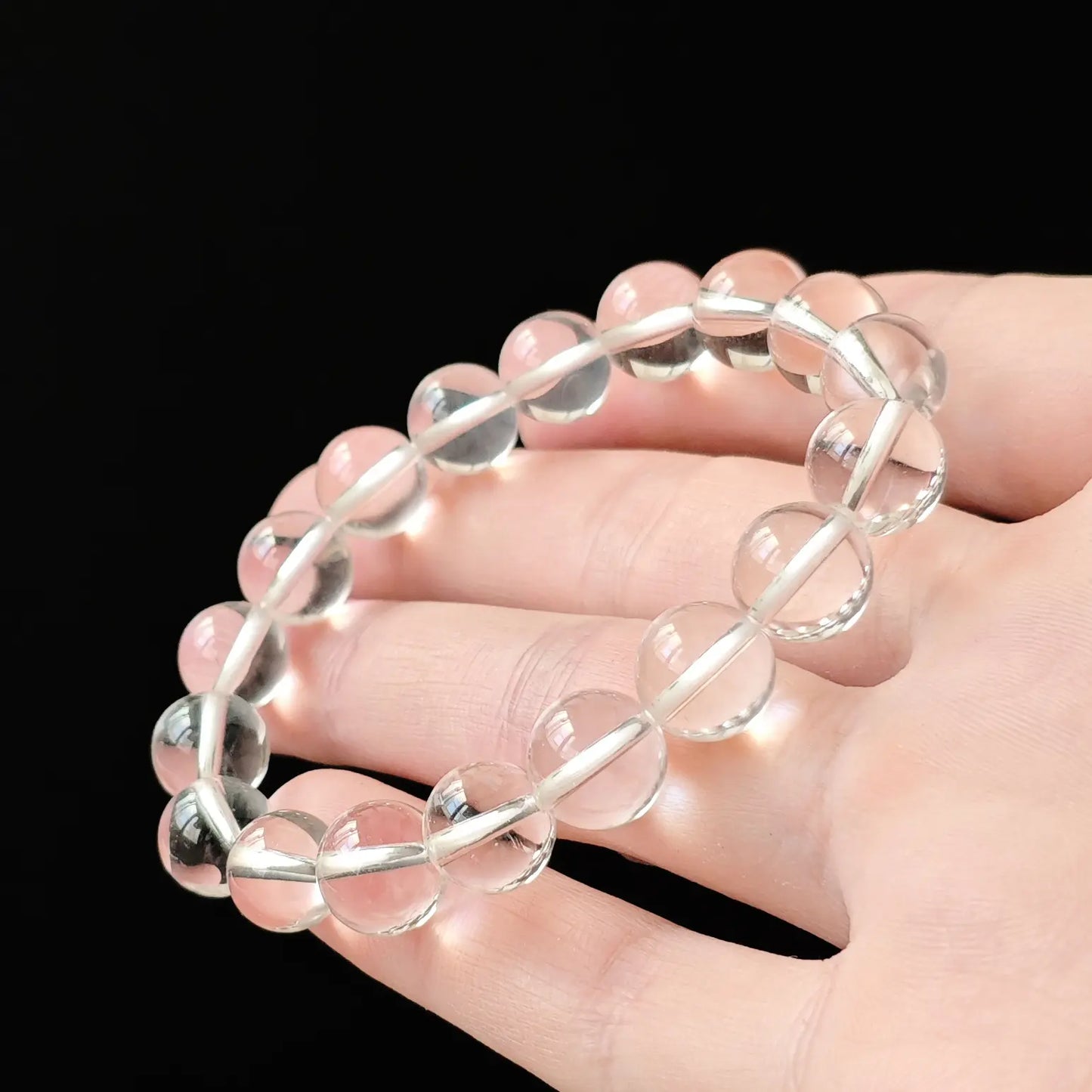 Hand holding near-perfect clear quartz bracelet to demonstrate light passing through beads—proof of high-grade inclusion-free quality, not cloudy or milky
