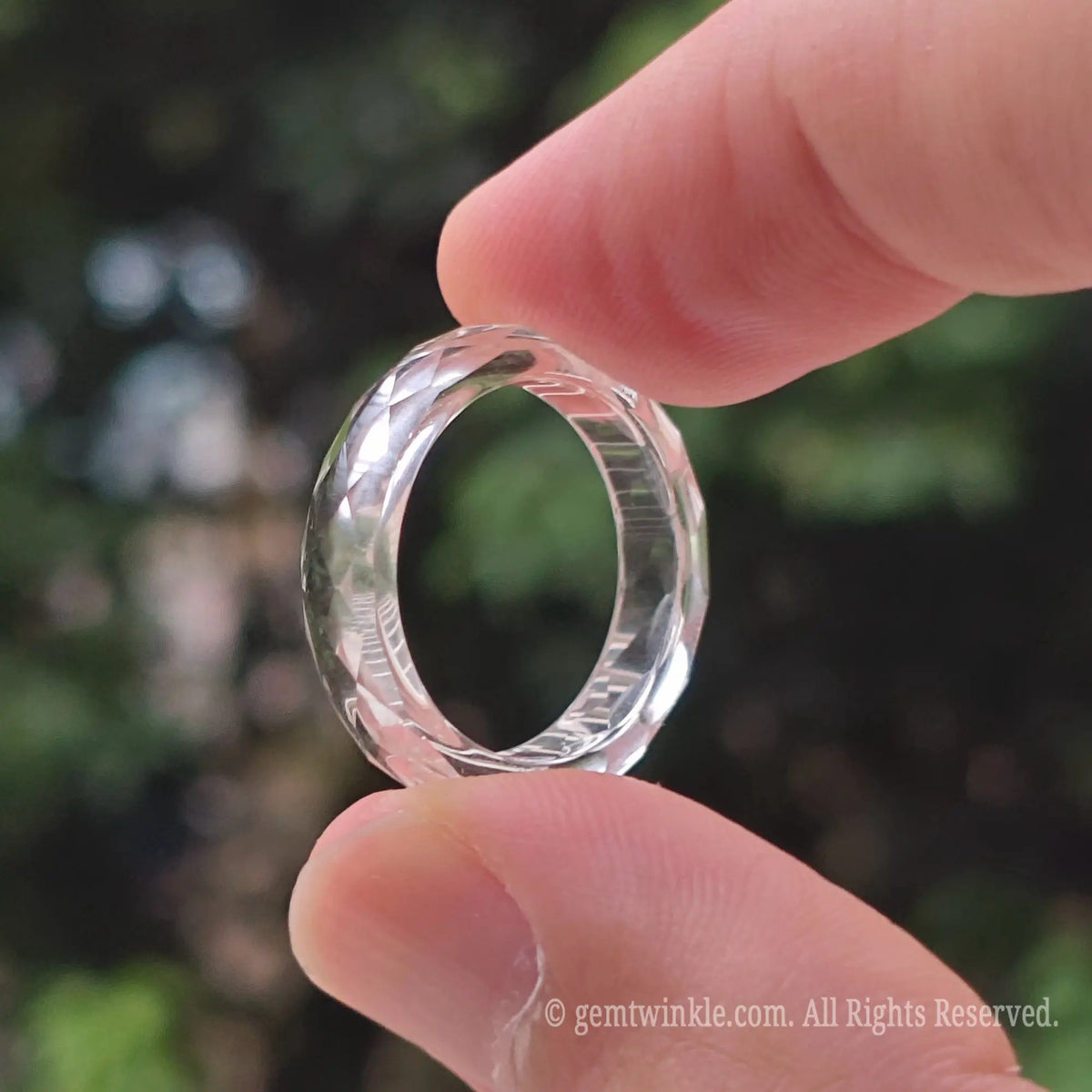 Close up view of transparent faceted clear quartz ring resting on fingers highlighting glittering geometric angles