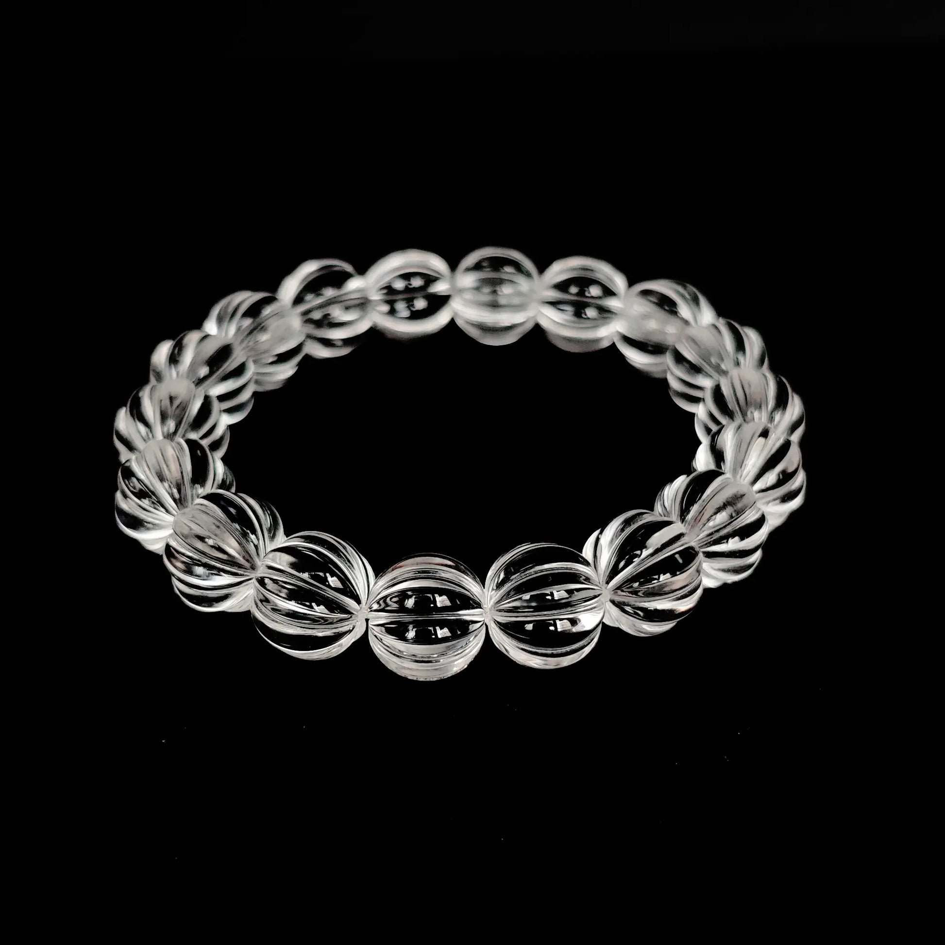 Natural clear quartz pumpkin-shaped bead bracelet laid flat on black background, showcasing full circle design and faceted transparency