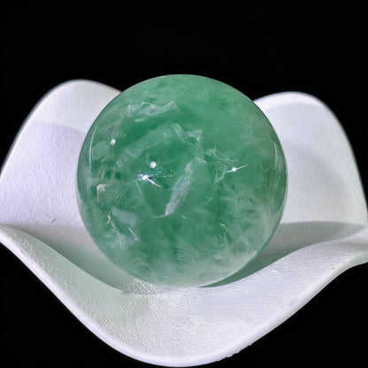 Close-up of green fluorite sphere showing layered white feather inclusions and smooth polished surface