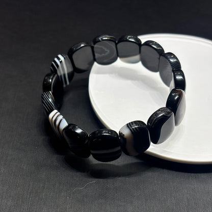Close-up of natural black and white banded onyx square beads, polished geometric edges and parallel banding pattern