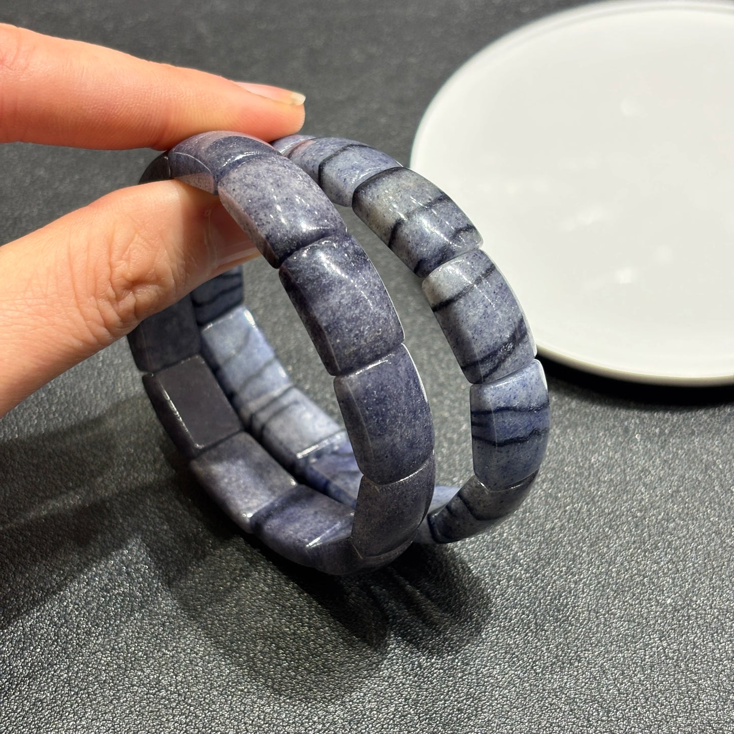 Hand holding two blue aventurine square tablet bracelets, showing bead thickness and stretch cord flexibility