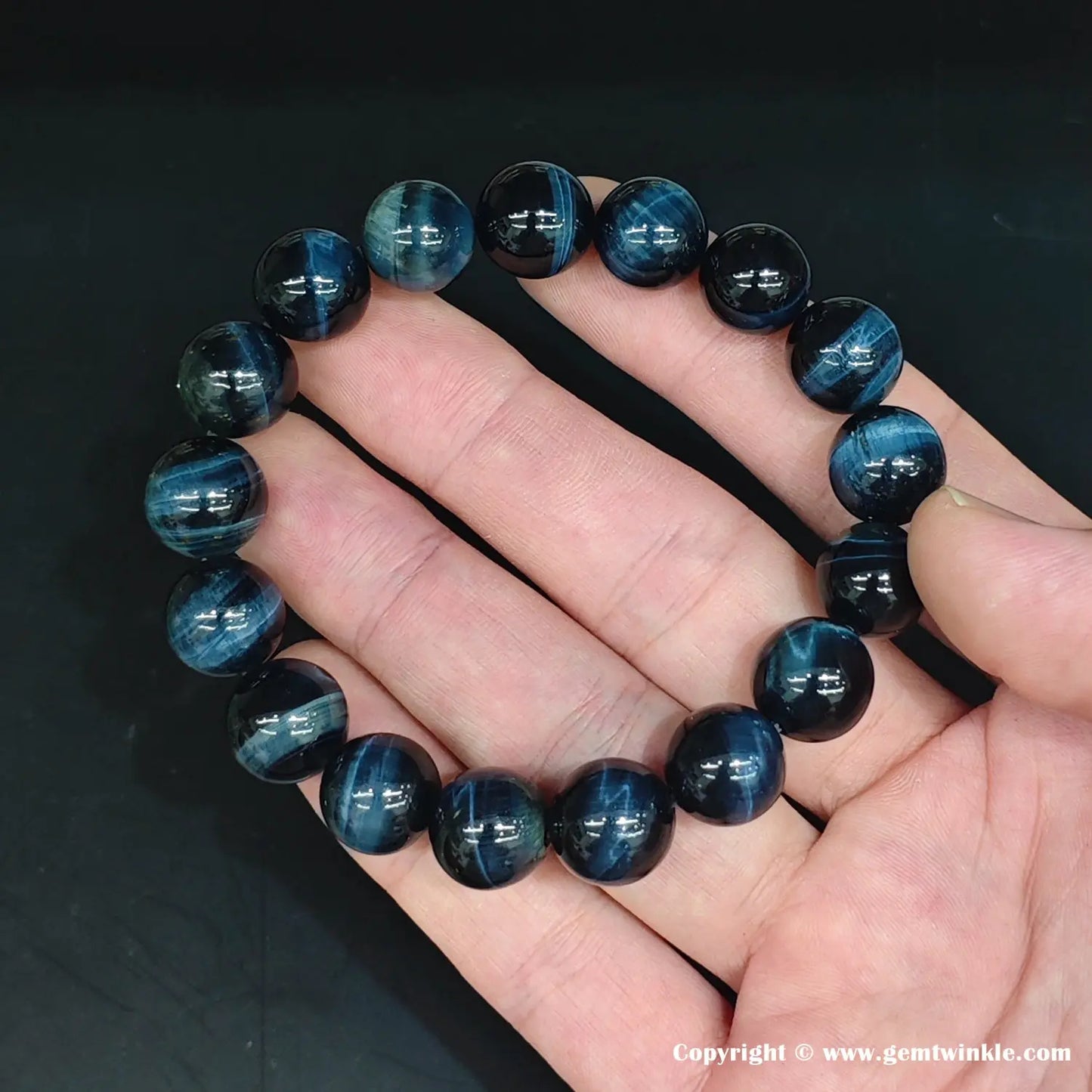 Macro detail of a ~10mm blue tiger’s eye round bead. The polished surface reveals intense chatoyant bands—bright sapphire-blue streaks moving across a deep navy matrix under direct light.