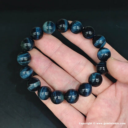 Macro detail of a ~10mm blue tiger’s eye round bead. The polished surface reveals intense chatoyant bands—bright sapphire-blue streaks moving across a deep navy matrix under direct light.
