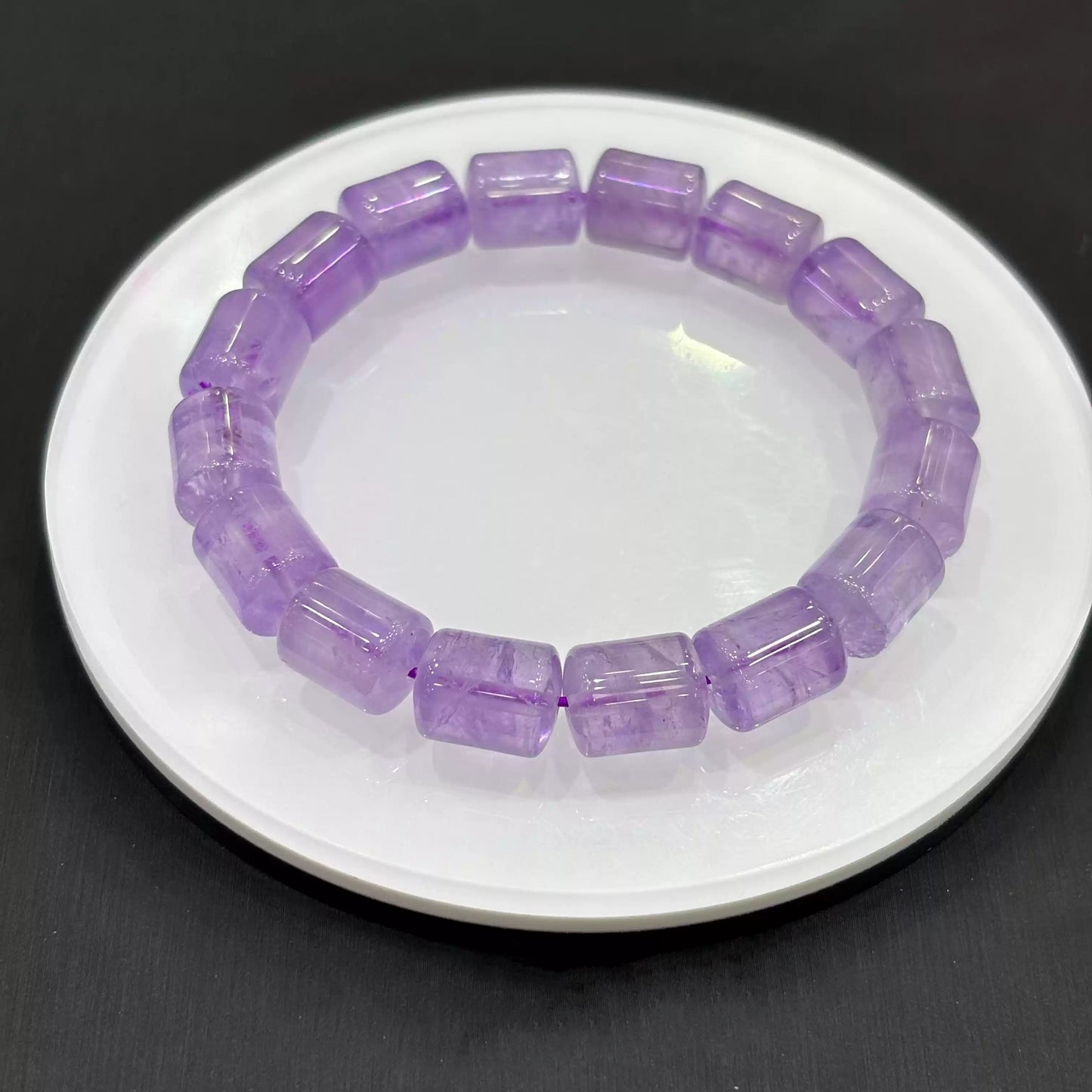 Angled close-up of a light purple amethyst crystal bracelet resting beside a white dish, revealing faceted edges, internal inclusions, and smooth polish of rectangular beads.
