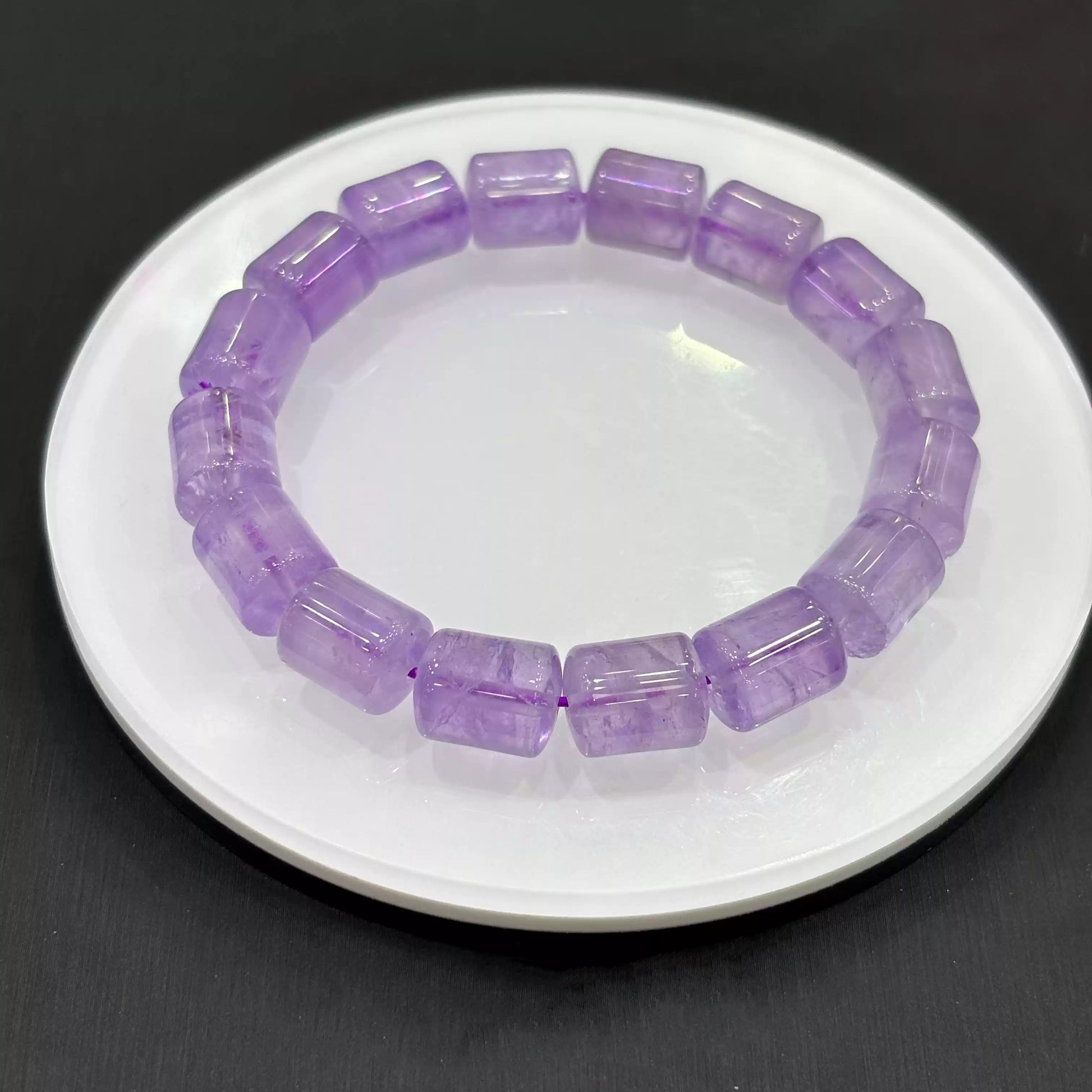 Angled close-up of a light purple amethyst crystal bracelet resting beside a white dish, revealing faceted edges, internal inclusions, and smooth polish of rectangular beads.