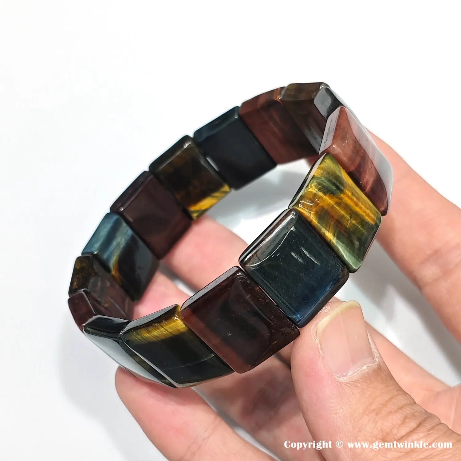 Hand displaying tiger eye bangle from side angle, emphasizing precise bead alignment, color zoning, and polished rectangular facets for retail display