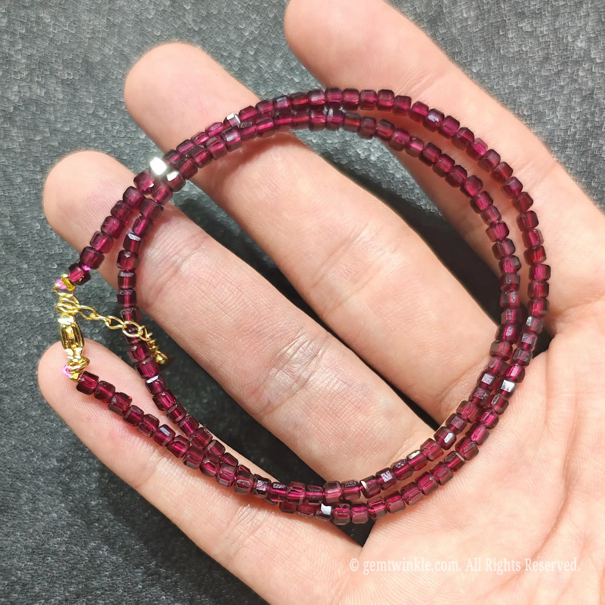 Coiled 3mm geometric cube cut Red Garnet necklace held across fingers suited for boutique store displays