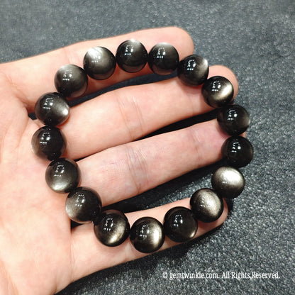 Full ring view of a premium select gray tone cat eye obsidian bracelet resting on textured gray fabric