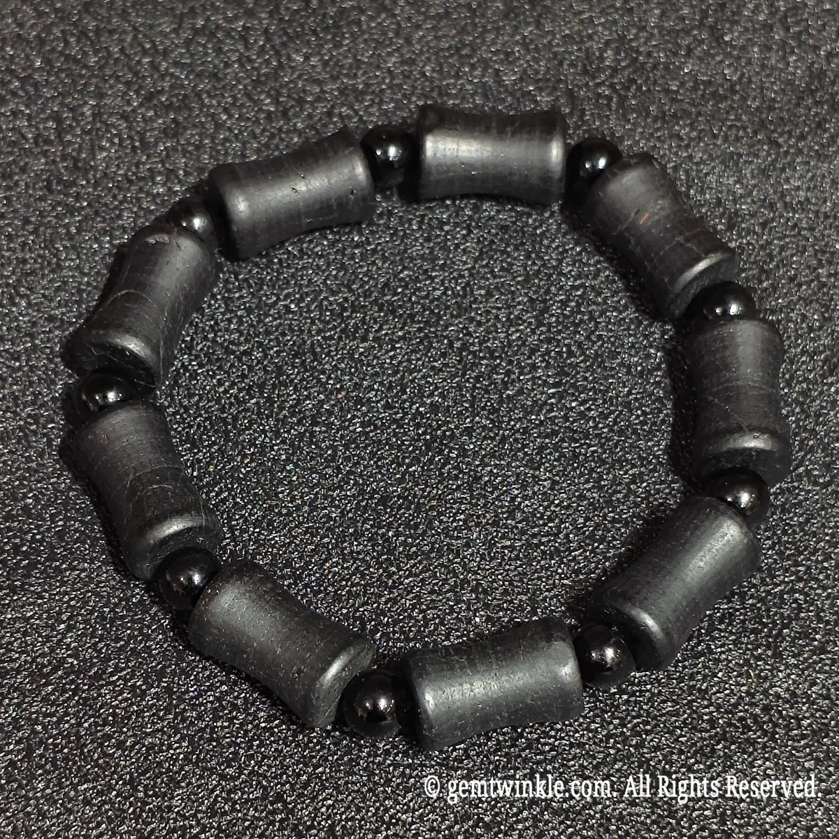 Perspective view of a natural matte black tourmaline barrel stretch bracelet highlighting organic mineral striations and dark luster