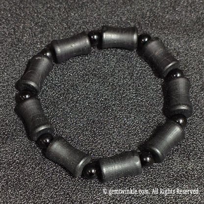 Perspective view of a natural matte black tourmaline barrel stretch bracelet highlighting organic mineral striations and dark luster