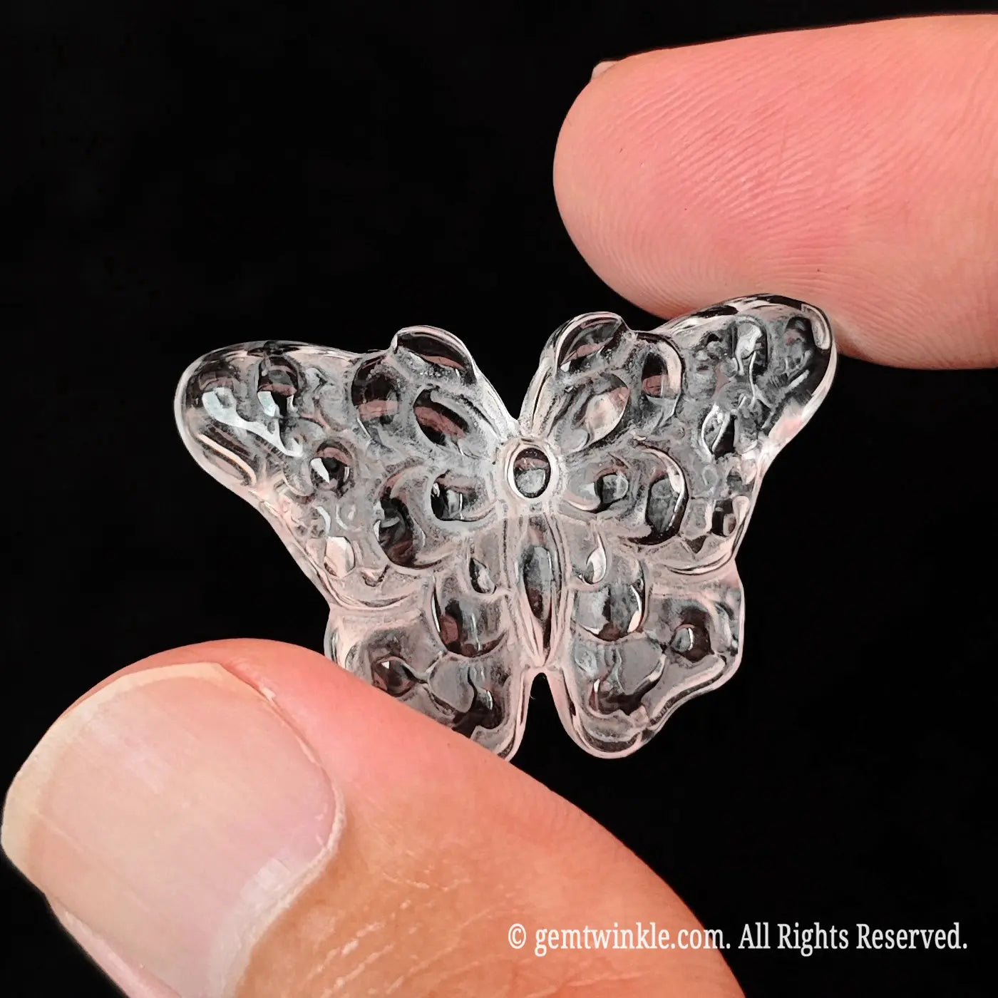 Side angle display of 3cm carved clear quartz butterfly resting between fingertips showing smooth polished flat backing