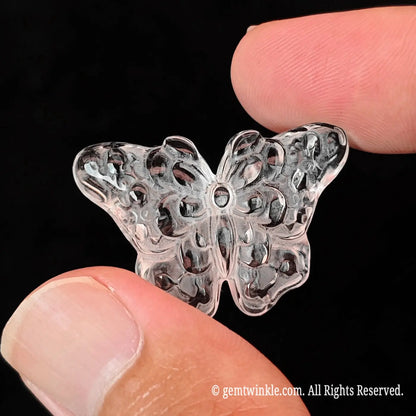 Side angle display of 3cm carved clear quartz butterfly resting between fingertips showing smooth polished flat backing