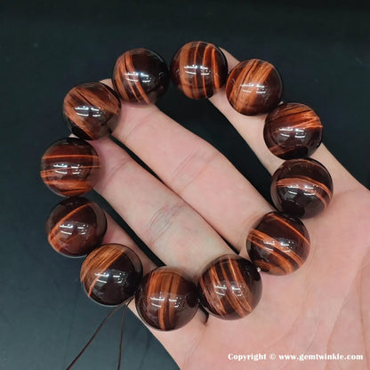 Two beads held side-by-side: a ~6mm and a ~20mm red tiger’s eye sphere, illustrating the full size spectrum available in this collection.