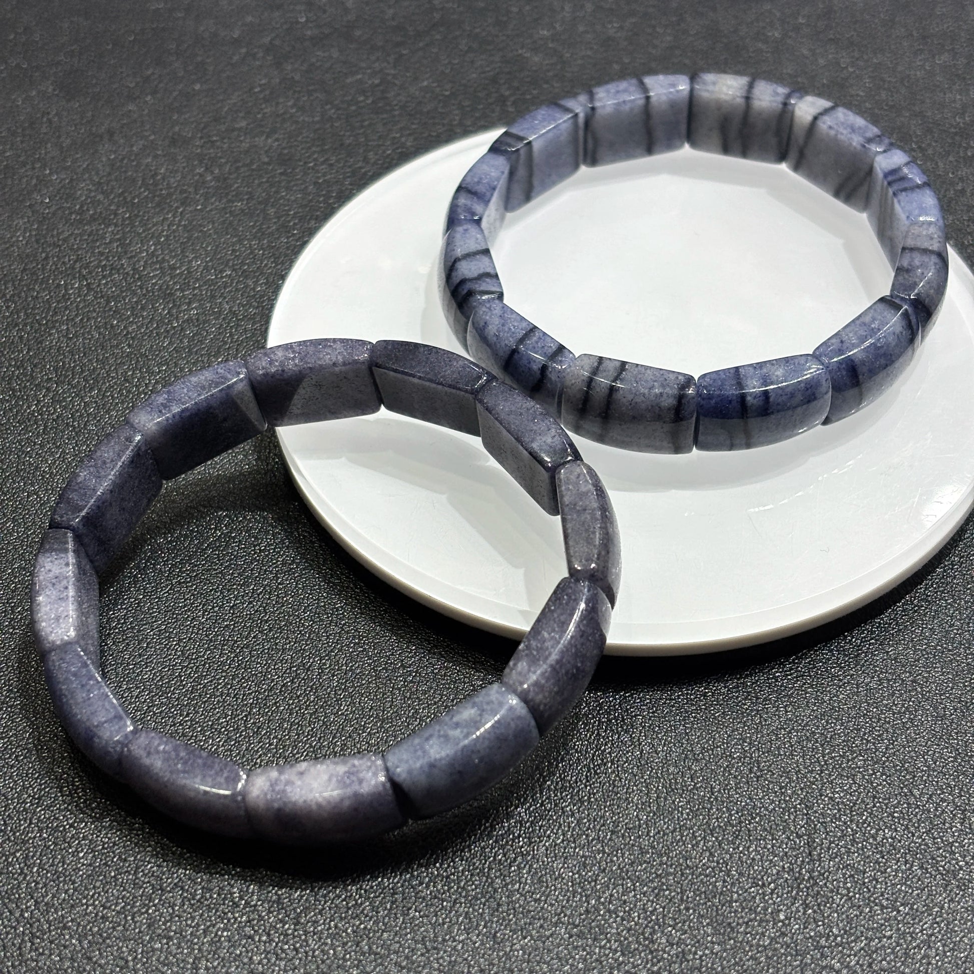 Blue aventurine square tablet bracelets crossed on dark surface, showcasing depth, transparency, and sparkle