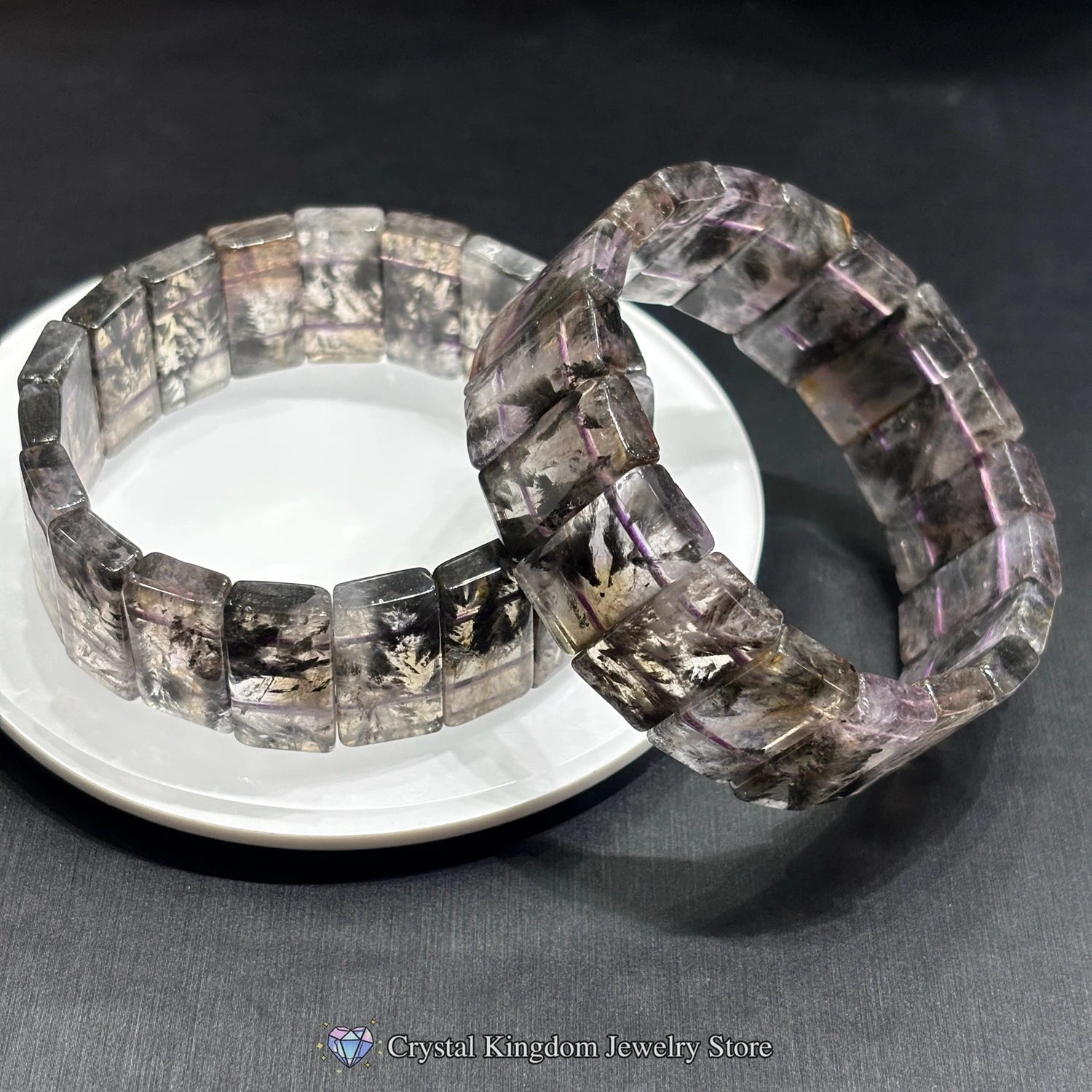 Two black dream phantom quartz rectangular slab bracelets crossed on white disc, minimalist artistic stacking jewelry