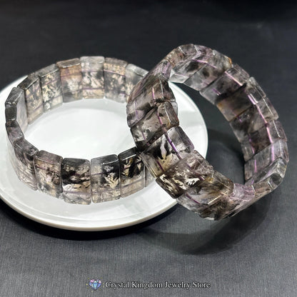 Two black dream phantom quartz rectangular slab bracelets crossed on white disc, minimalist artistic stacking jewelry
