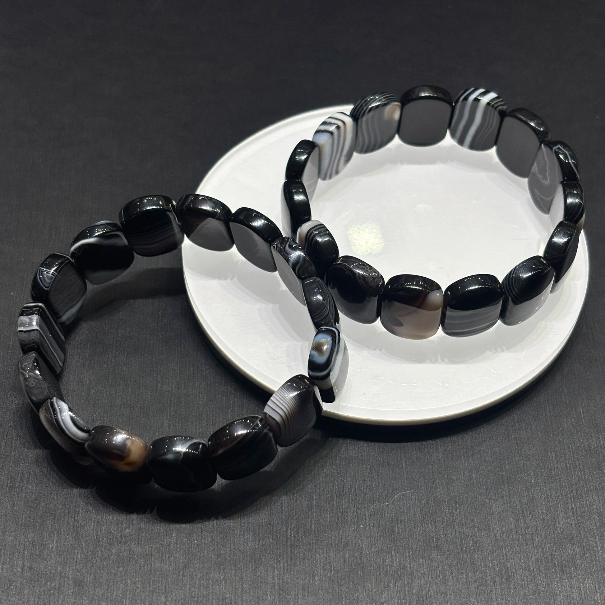 Black and white banded onyx square bead bracelets crossed on dark surface, stylish aesthetic casual wear jewelry