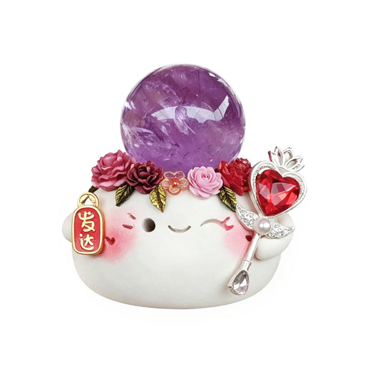 Adorable white clay figurine with smiling face, wearing floral crown and holding “Fa Da” charm, topped with natural amethyst sphere.