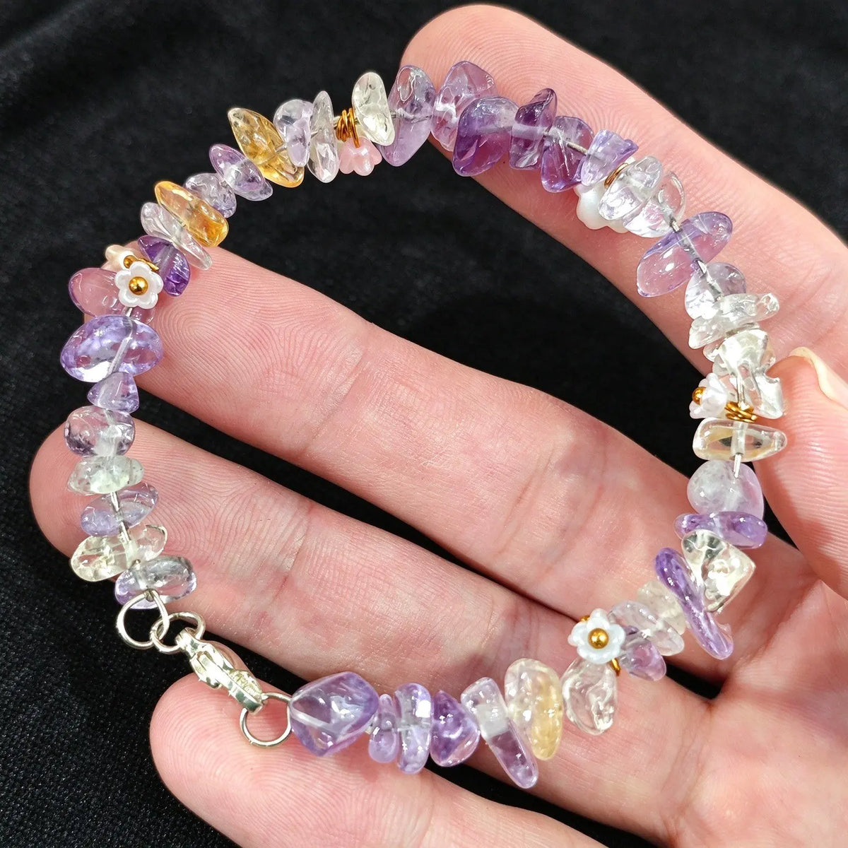 Hand holding a delicate non elastic amethyst and citrine chip stone wire wristband displaying metal clasp fastening