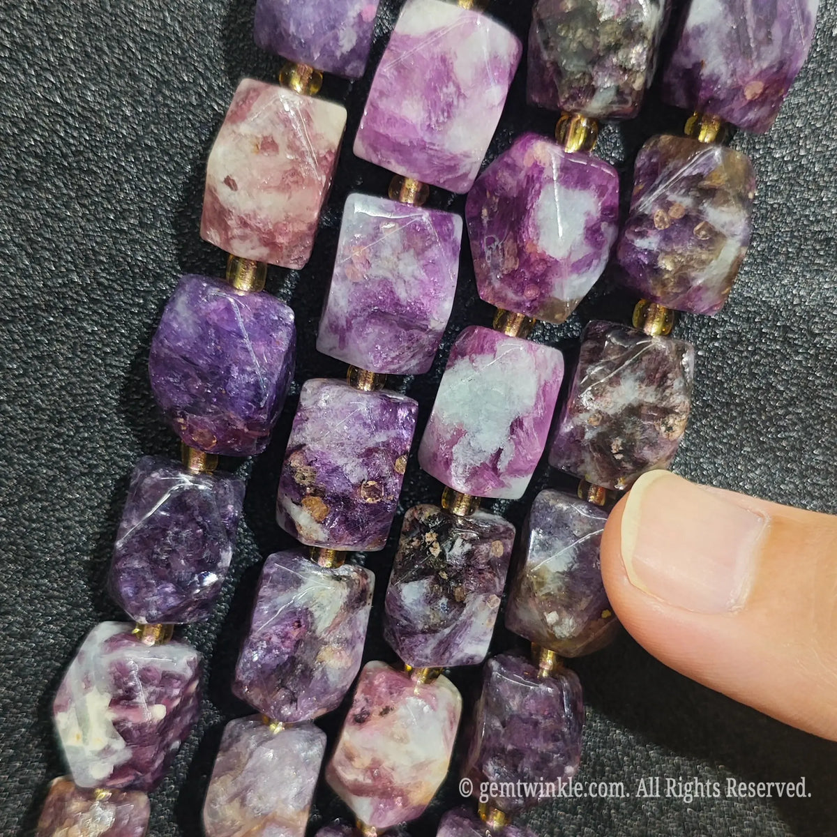 Hand holding four strands of natural royal violet lepidolite faceted freeform beads showing rich purple color