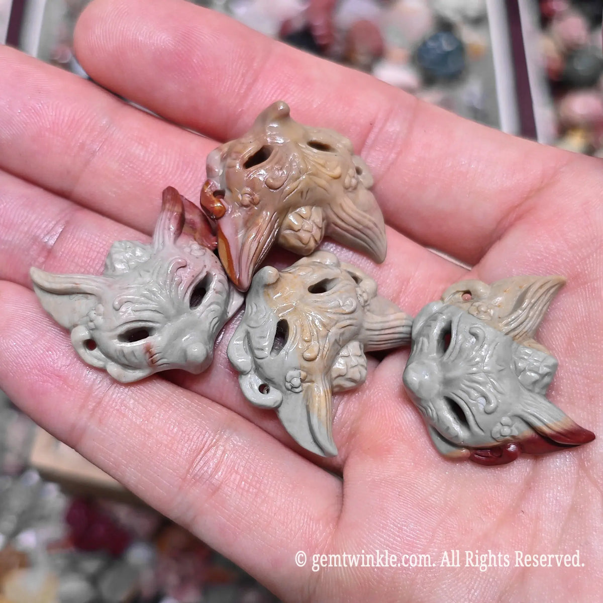 Close up view of natural multi color Alxa agate fox mask carved statues resting on hand highlighting polished surface