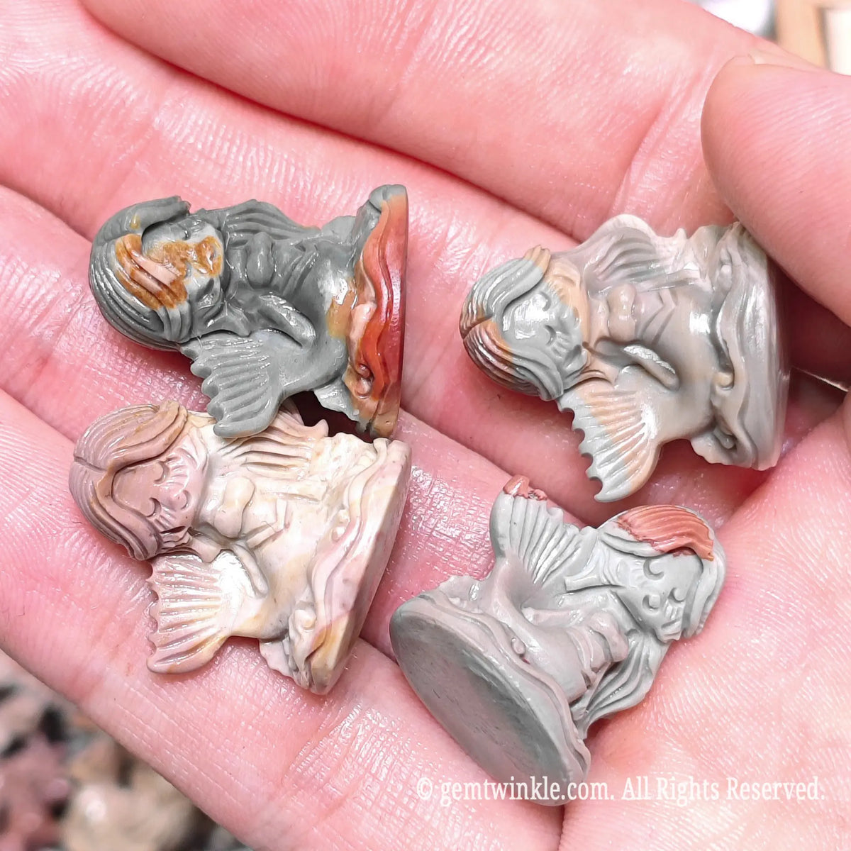 Close up view of natural multi color Alxa agate mermaid carved statues resting on hand highlighting smooth finish