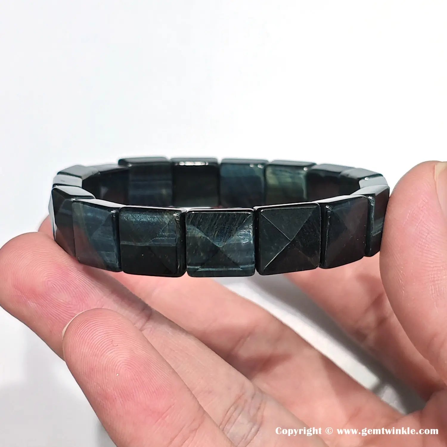 Macro view showing the precise triangular facets and sharp edges of the pyramid-cut blue tiger eye beads, highlighting the craftsmanship and light reflection.