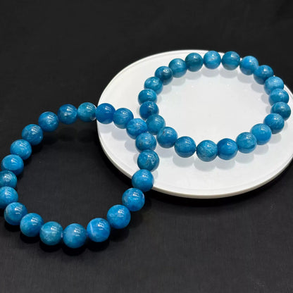 Two natural blue apatite bracelets overlapping on white dish under soft studio light, emphasizing depth and clarity of the stone