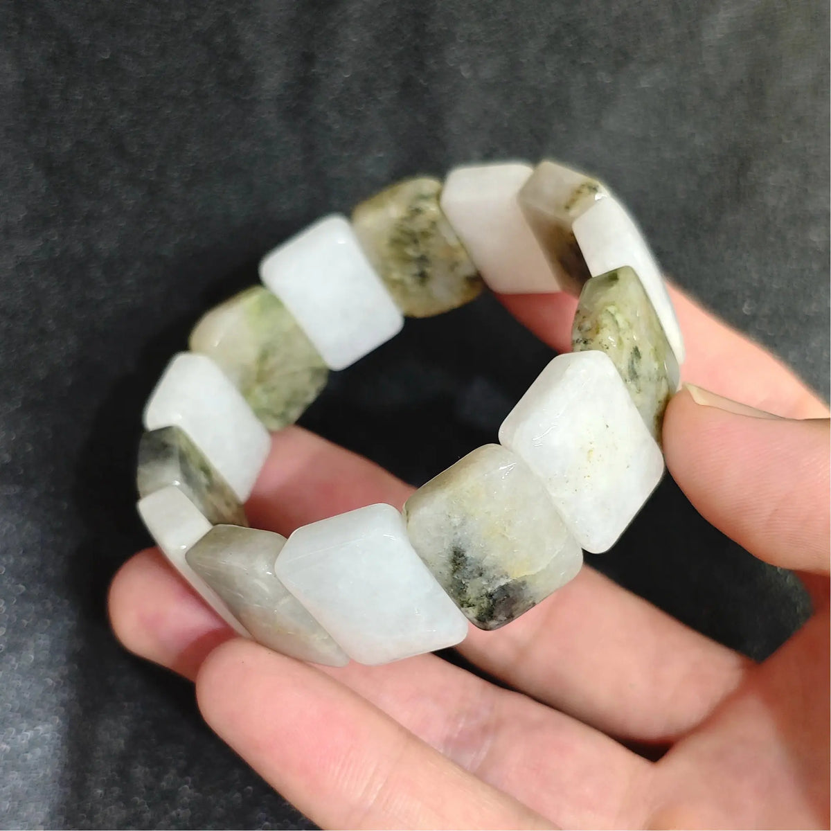 Natural snowy white golden jadeite quartz smooth segment stretch bracelet held on hand displaying milky base and moss green inclusions