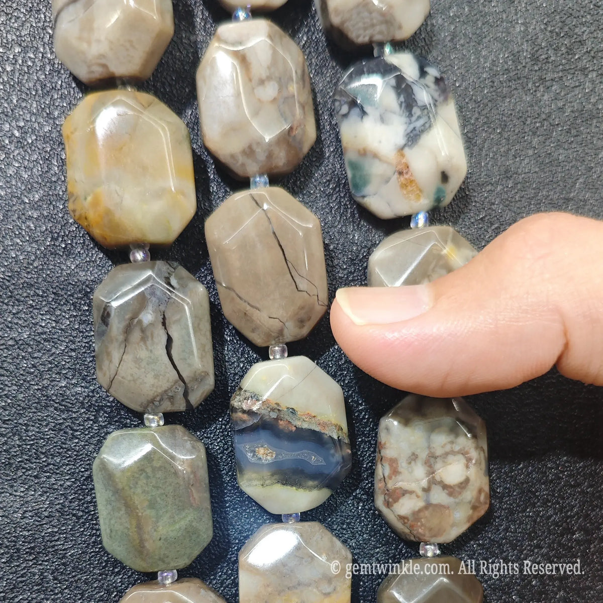 Hand displaying natural volcanic ash agate faceted flat slab beads showing smoky tan and grey color layering