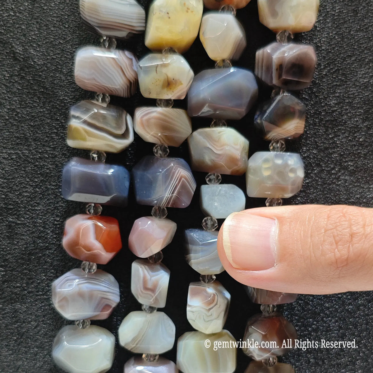 Side view of natural crazy lace agate faceted pebble beads strung on loose strands showing earthy swirls and lace patterns