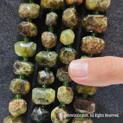 Close up view of natural olive green garnet faceted nugget beads highlighting refractive facets and natural earthy crust