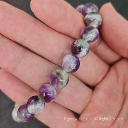 Close up view of 10mm feather fluorite crystal bracelet resting on palm highlighting feathery mineral patterns