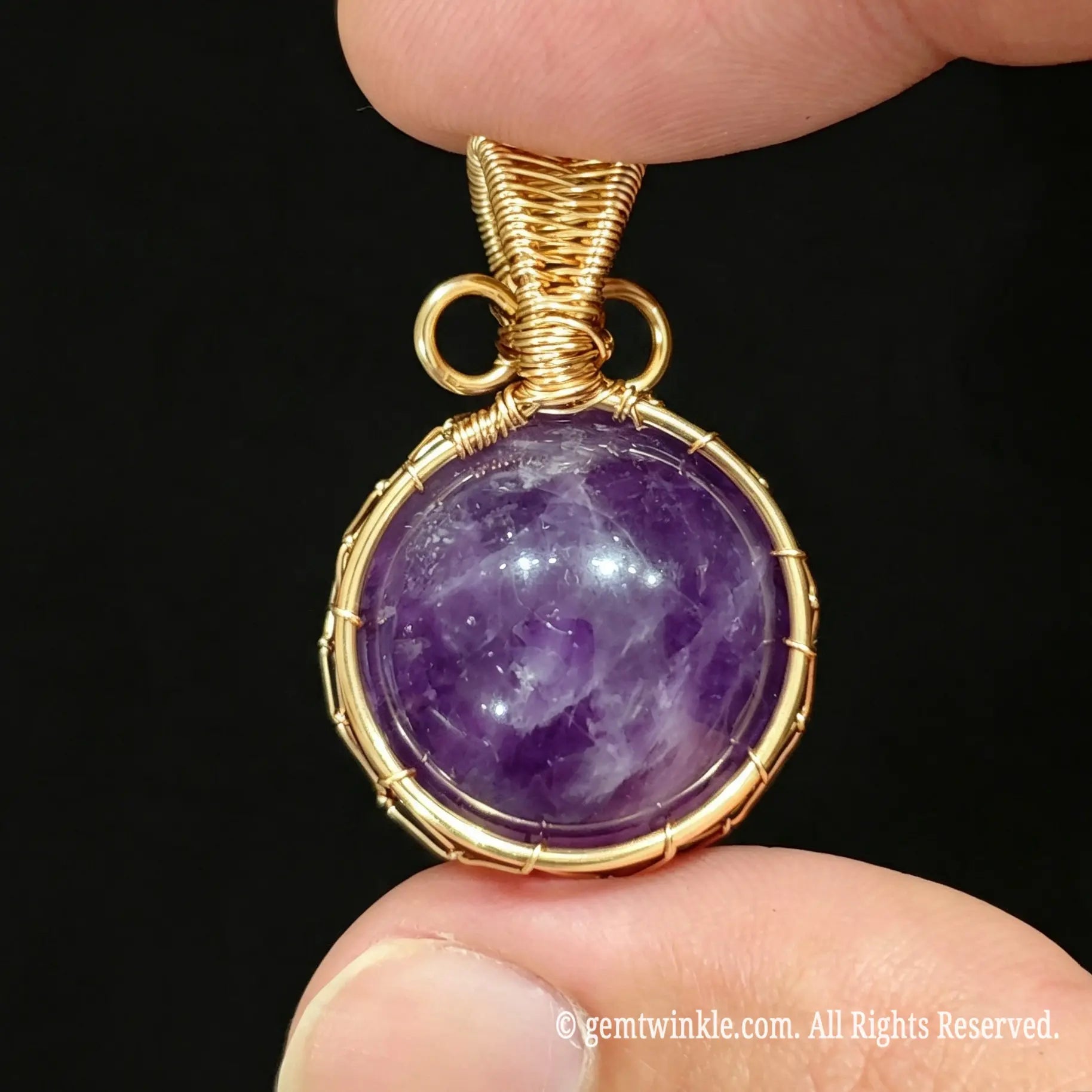 Front view of gold wire wrapped purple amethyst sphere pendant held in hand showing intricate net structure