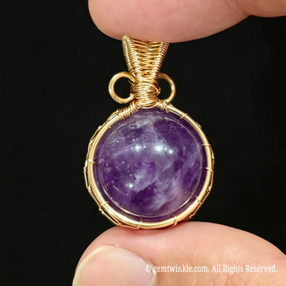 Front view of gold wire wrapped purple amethyst sphere pendant held in hand showing intricate net structure