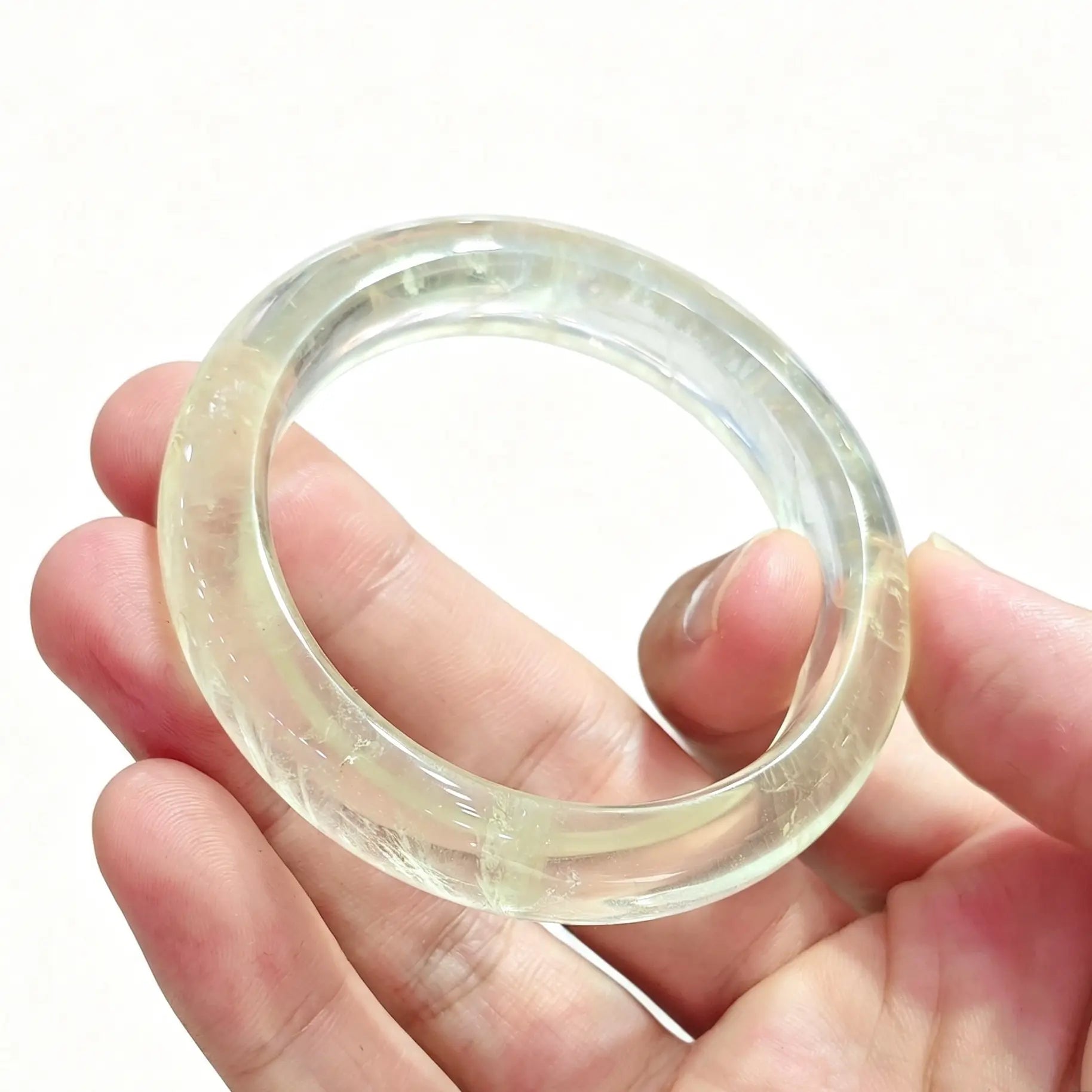 Angled hand view of a smooth round lemon quartz bangle showing bright golden-yellow luster