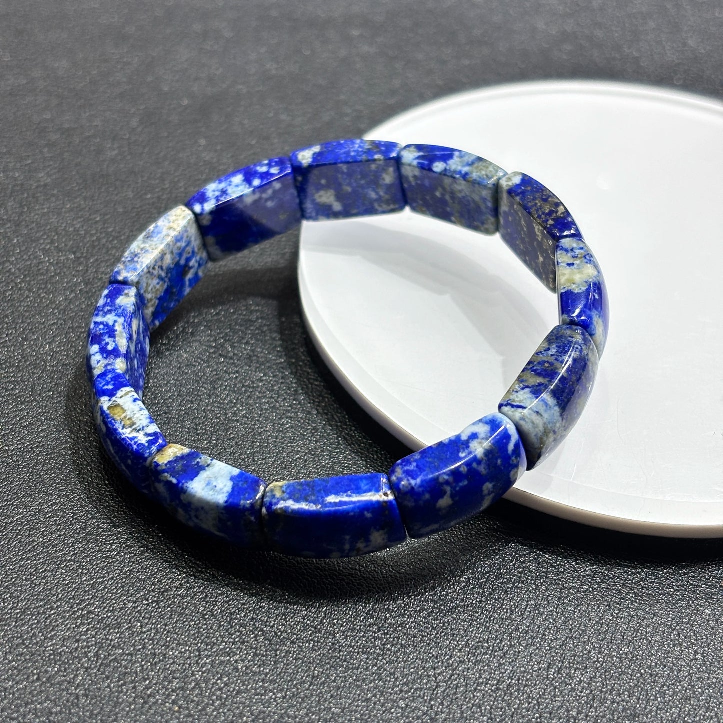 Top-side view of natural lapis lazuli square bead bracelet on white dish; highlights smooth edges, pyrite flecks, and stone texture