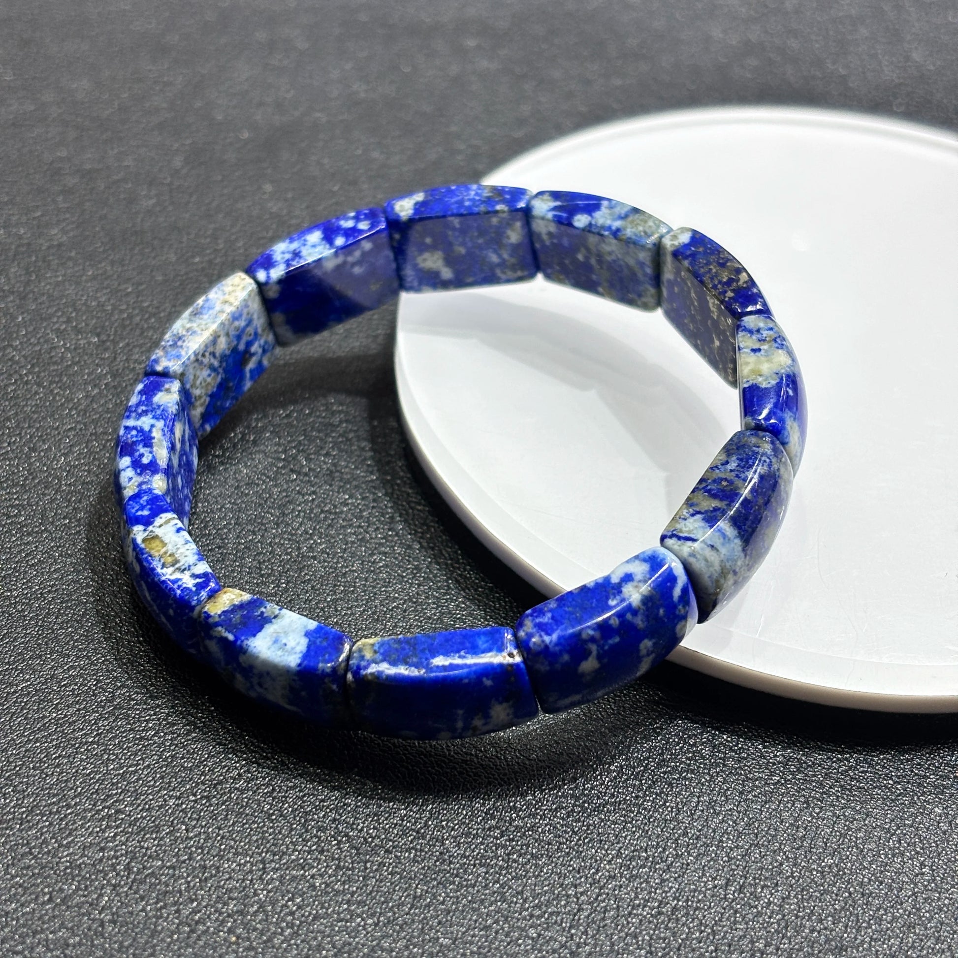 Top-side view of natural lapis lazuli square bead bracelet on white dish; highlights smooth edges, pyrite flecks, and stone texture