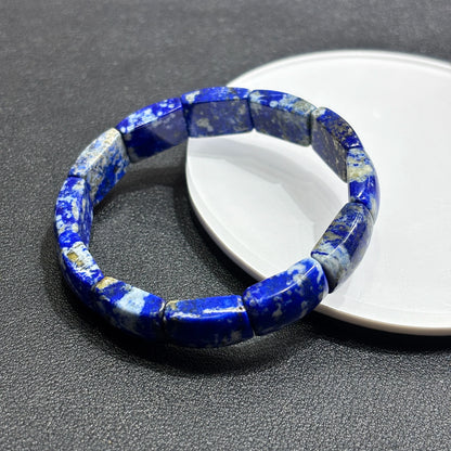 Top-side view of natural lapis lazuli square bead bracelet on white dish; highlights smooth edges, pyrite flecks, and stone texture