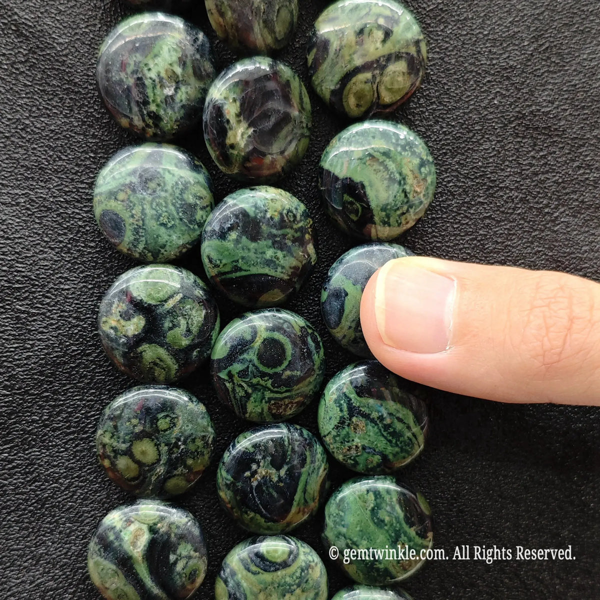 Side view of natural peacock eye stone coin disc beads strung on loose strands showing green and black whorls