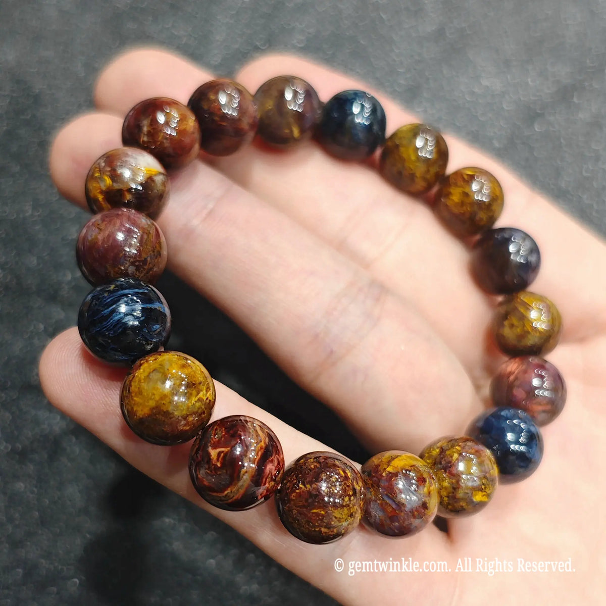Fingertips holding a 10mm pietersite chatoyant beaded wristlet displaying earthy yellow and navy blue patches