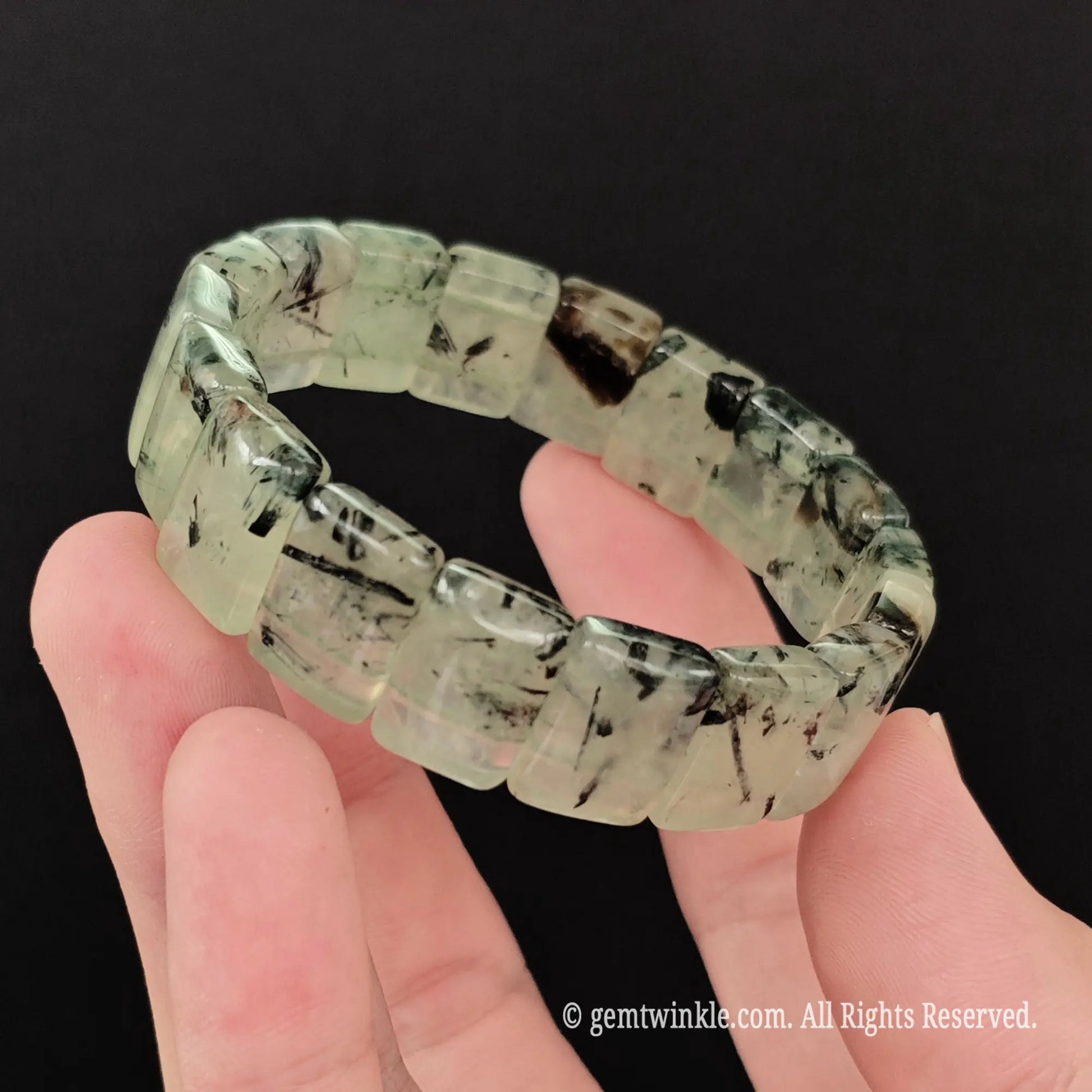 Full view of translucent prehnite tourmaline needles block bead bracelet held open in hand showing dual stretch cord structure