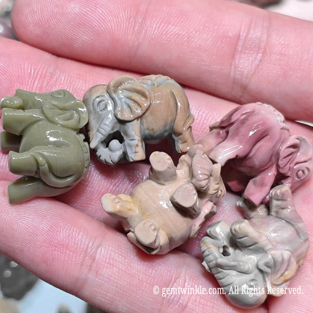 Close up view of natural multi color Alxa agate elephant carved statues resting on hand highlighting smooth rounded contours