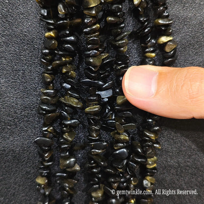Fingers holding shimmering natural golden obsidian gemstone chip beads on black background[cite: 9]
