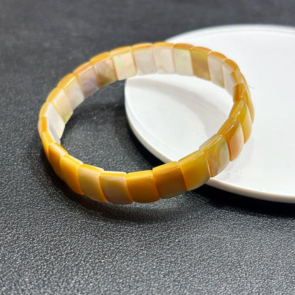 Close-up of natural golden shell rectangle bead showing iridescent sheen and organic color gradient; evokes calm abundance and natural rhythm