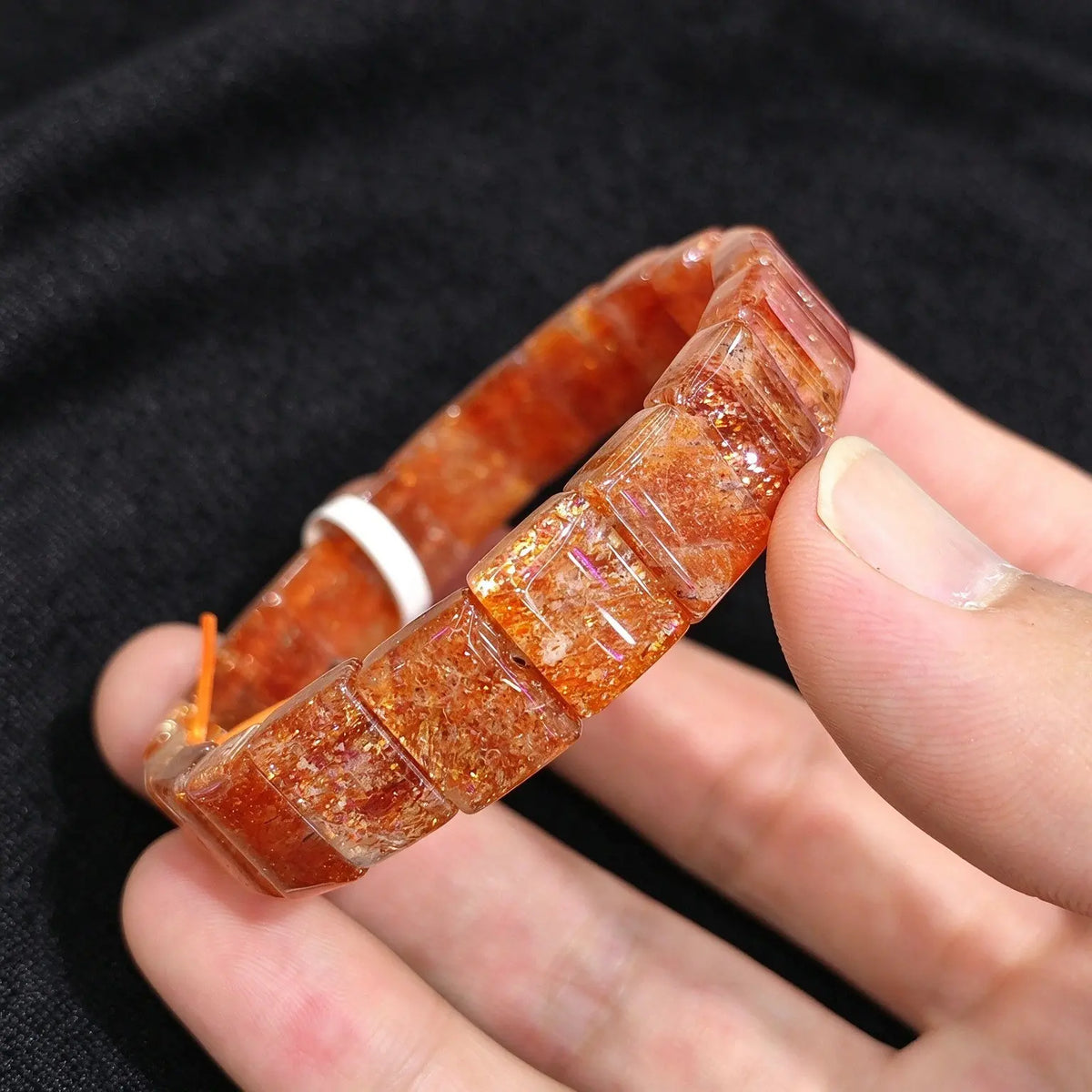Hand displaying a high grade golden sunstone smooth block tile stretch bracelet showing rich orange red feldspar and golden schiller sparkles