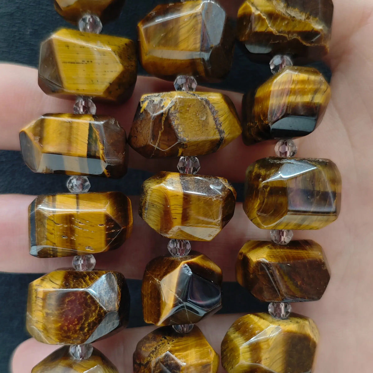 Close up perspective of multiple natural golden tiger eye freeform faceted bead strands showing golden flash