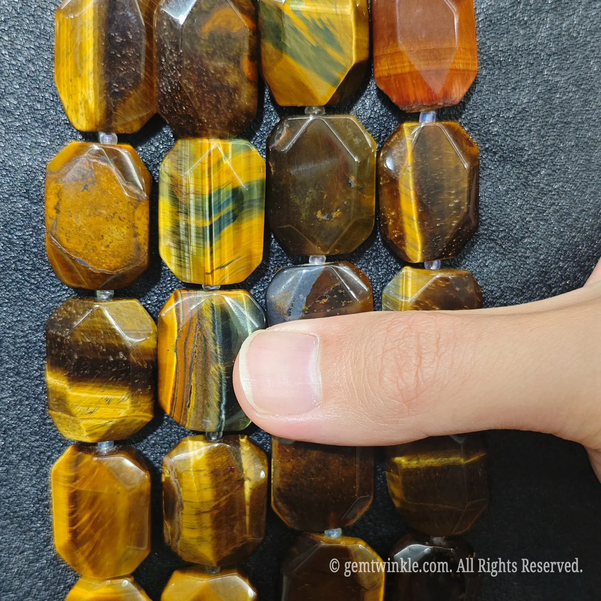 Close up perspective of multiple golden tiger eye faceted flat slab bead strands aligned on dark surface