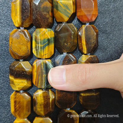 Close up perspective of multiple golden tiger eye faceted flat slab bead strands aligned on dark surface